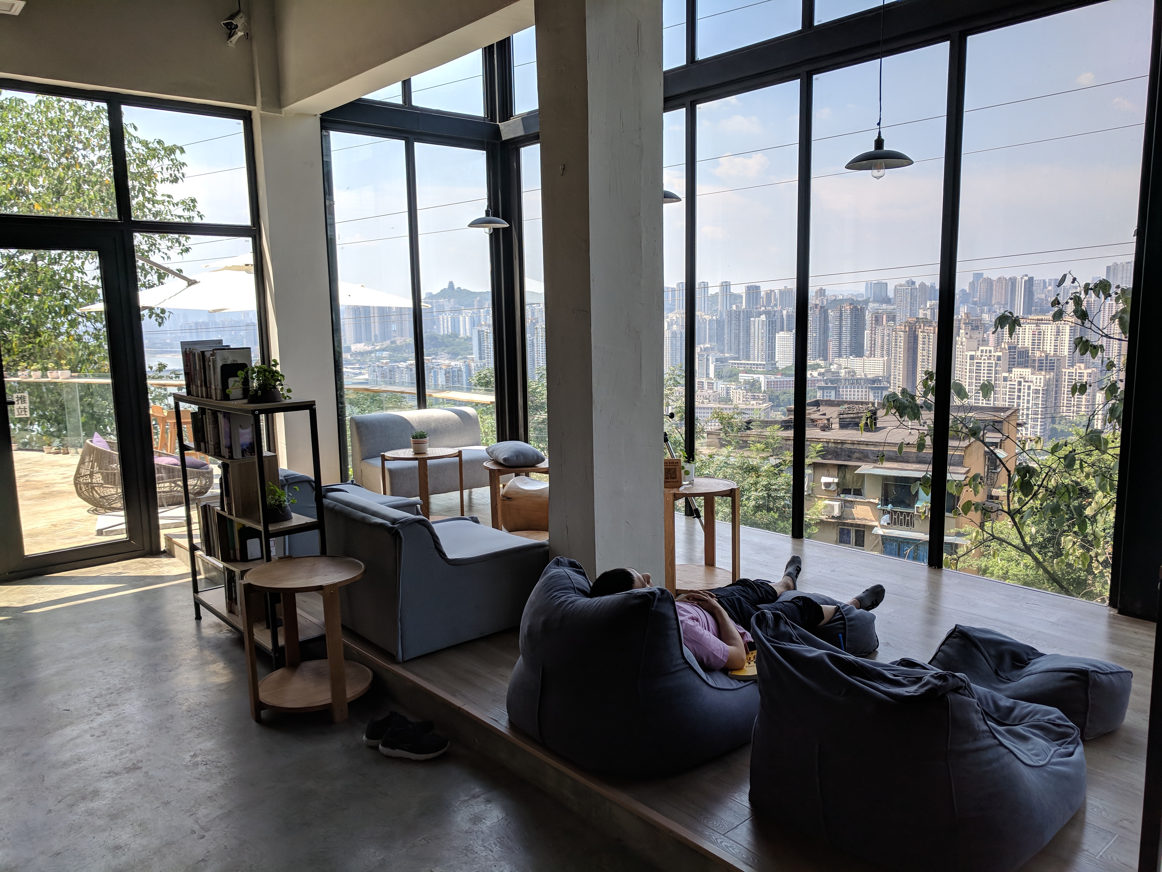 A man relaxes on a bean bag bed surrounded by windows overlooking the city